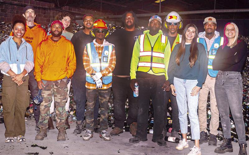 Glass Half Full staff stands in front of pile of glass waiting to be crushed in their warehouse.