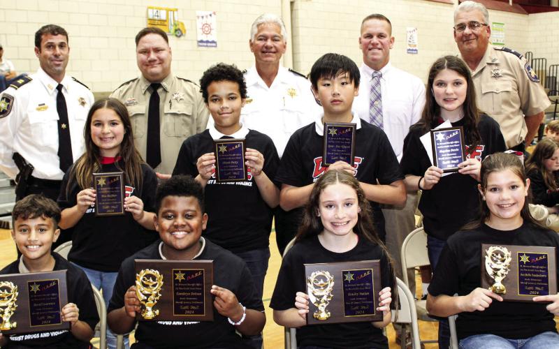 Arabi Elementary School fifth graders named St. Bernard Sheriff’s Office D.A.R.E. program first-place essay contest winners are, first row, from left: David Lourenco, Cambryn Dotson, Kinsley Nation and Ava Bella Vandenborre. Second-place winners are second row, from left: Mia Heffker, Elijah Petty, Quot-Viet Nguyen and Hayden Davis. With the winners are, third row, from left: Capt. Matthew Arcement, Sgt. Brandon Lewis, Sheriff James Pohlmann, Maj. Daniel Bostic and Lt. Robert Broadhead.