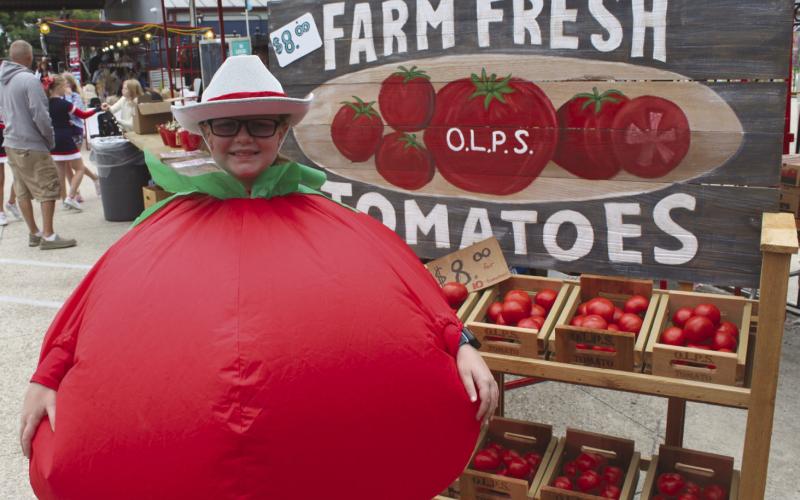 2024 Tomato Festival Mascot Emma Paisant-Pierson next to local and fresh farm tomatoes for sale.