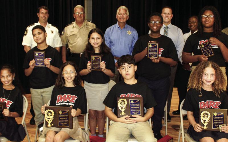Arlene Meraux Elementary School fifth graders named St. Bernard Sheriff’s Office D.A.R.E. program firstplace essay winners are first row, from left: Mya Jackson, Abigail Bazile, Layth Abumahfouz and Dia’mond Brown. Second-place winners are second row, from left: Joshua Serigne, Haisley Holden, Faizon Brown and Rachel Walker. With the winners are, third row, from left: Capt. Matthew Arcement, Lt. Robert Broadhead, Sheriff James Pohlmann, Maj. Daniel Bostic, Capt. Lisa Jackson and Sgt. Brandon Lewis.