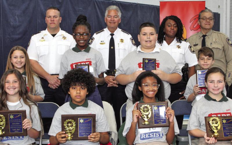 Joseph Davies Elementary School held a graduation Dec. 12 for fifth graders who graduated from the St. Bernard Sheriff’s Office D.A.R.E. program. First-place essay contest winners are, first row, from left: Aubrey Robin, Nathaniel Landry, Morgan Brisco and Jorja Hentze. Second-place essay contest winners are, second row, from left: Chloe Lafrance, Tyonne King, Baron Shano and Liam Jaufre. Third row, from left, are: Maj. Daniel Bostic, Sheriff James Pohlmann, Capt. Lisa Jackson and Sgt. Darrin Miller.