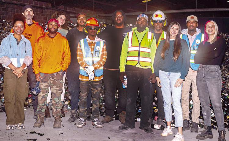 Glass Half Full staff stands in front of pile of glass waiting to be crushed in their warehouse.