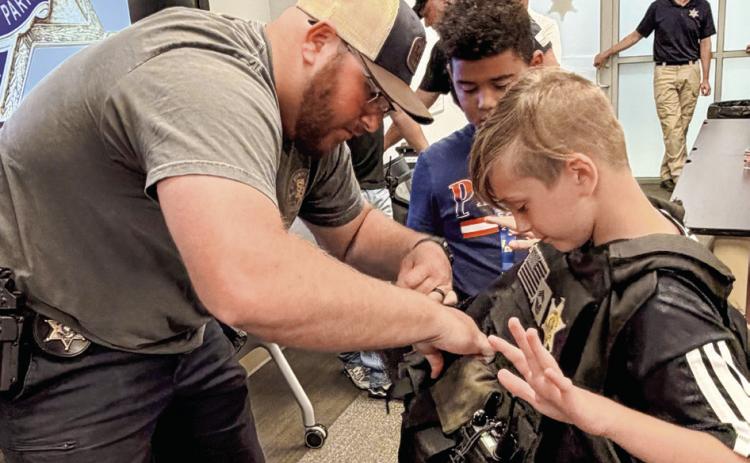 SBSO Narcotics Agent Rhett Fleetwood helps a Junior Deputy try on a protective law enforcement vest.
